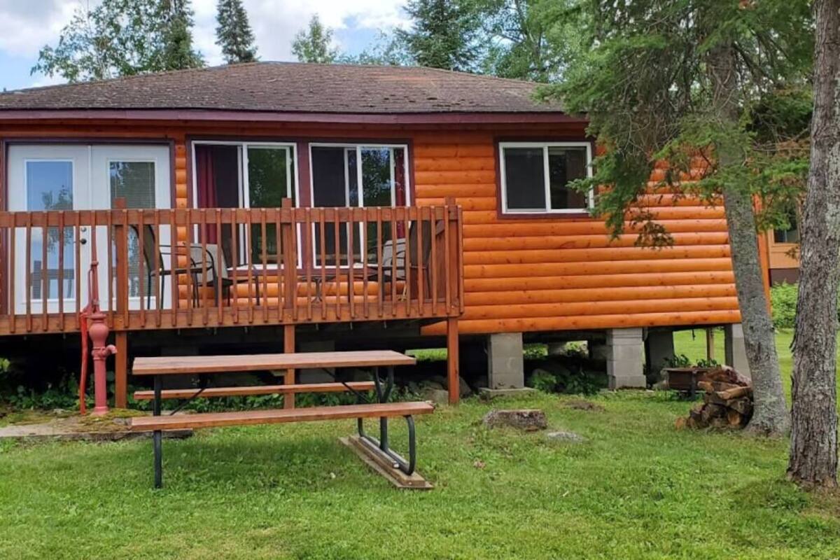 Une cabane en rondins avec une terrasse, une table de pique-nique et un petit coin jardin.