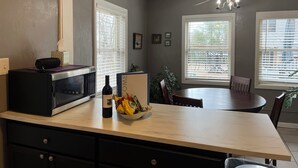 A kitchen with a microwave, a wine bottle, and a bowl of snacks on the counter.