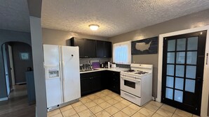 A compact kitchen with a refrigerator, stove, sink, and black cabinets.