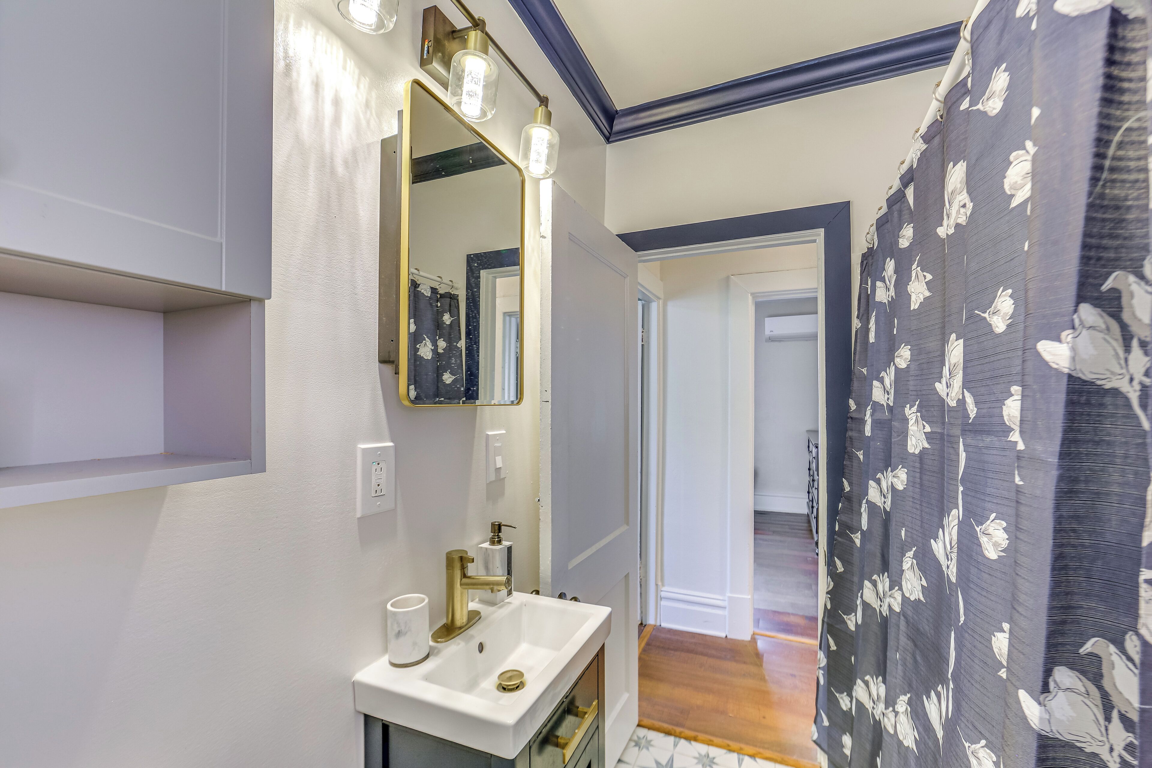 A bathroom with a white sink, a mirror with lights, and a shower curtain with a floral pattern.