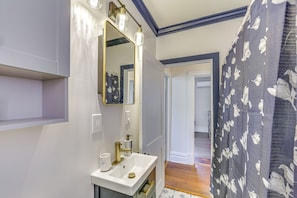 A bathroom with a white sink, a mirror with lights, and a shower curtain with a floral pattern. - Dog-friendly Pittsburgh Home, 3 Mi to Downtown! (Pittsburgh)