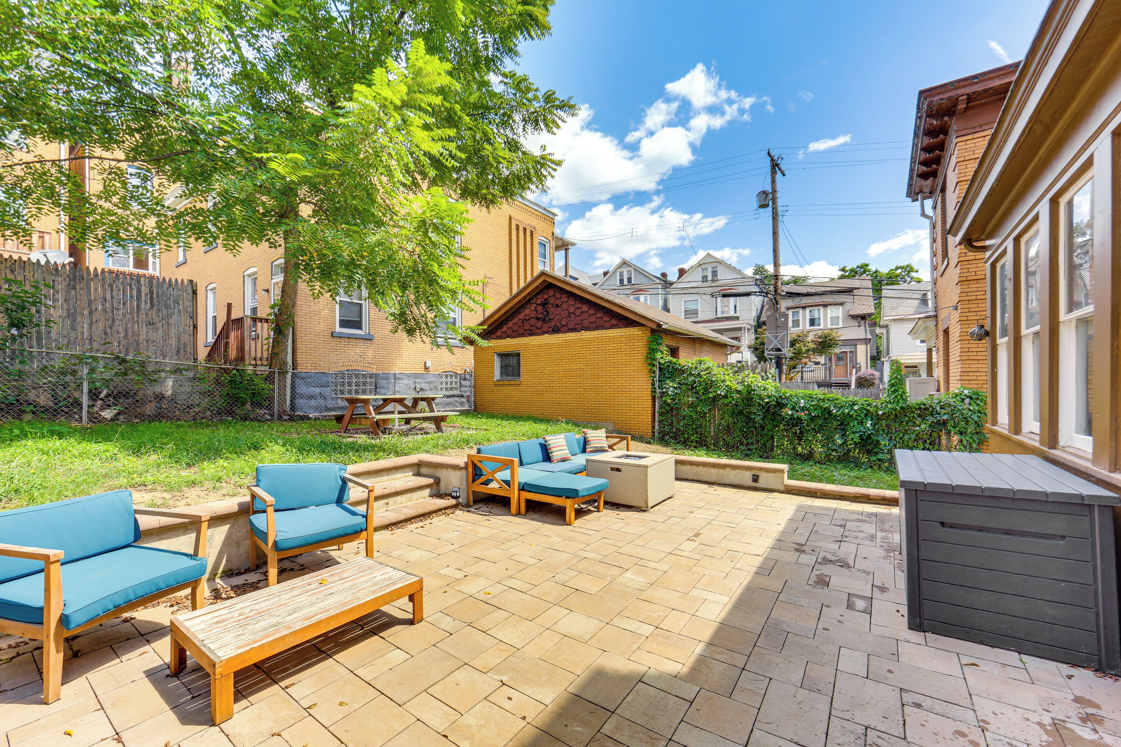 A patio with outdoor furniture, a wooden table, and a small brick building in the background.