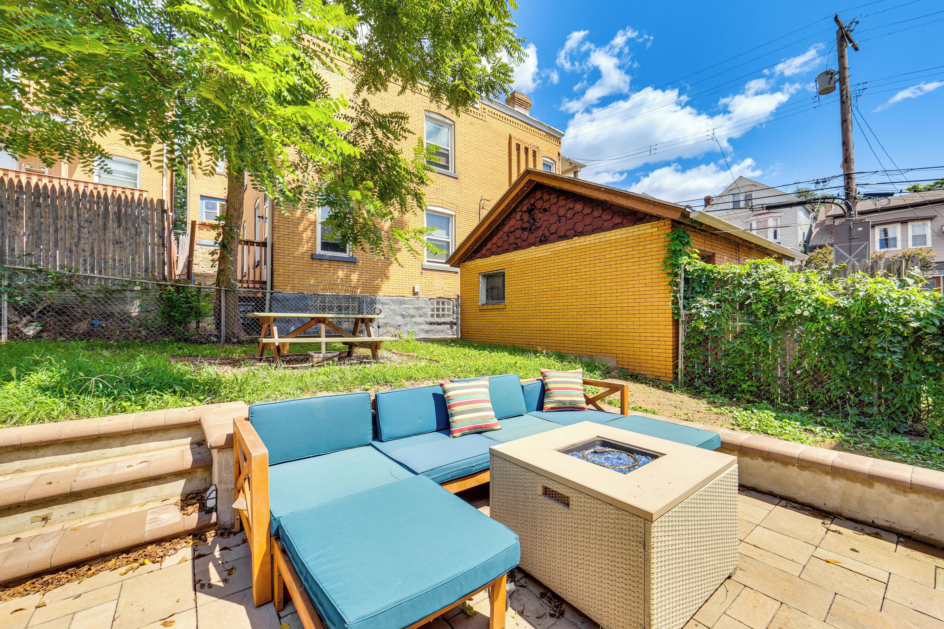 A patio area with a sofa set, a fire pit, and a wooden table.