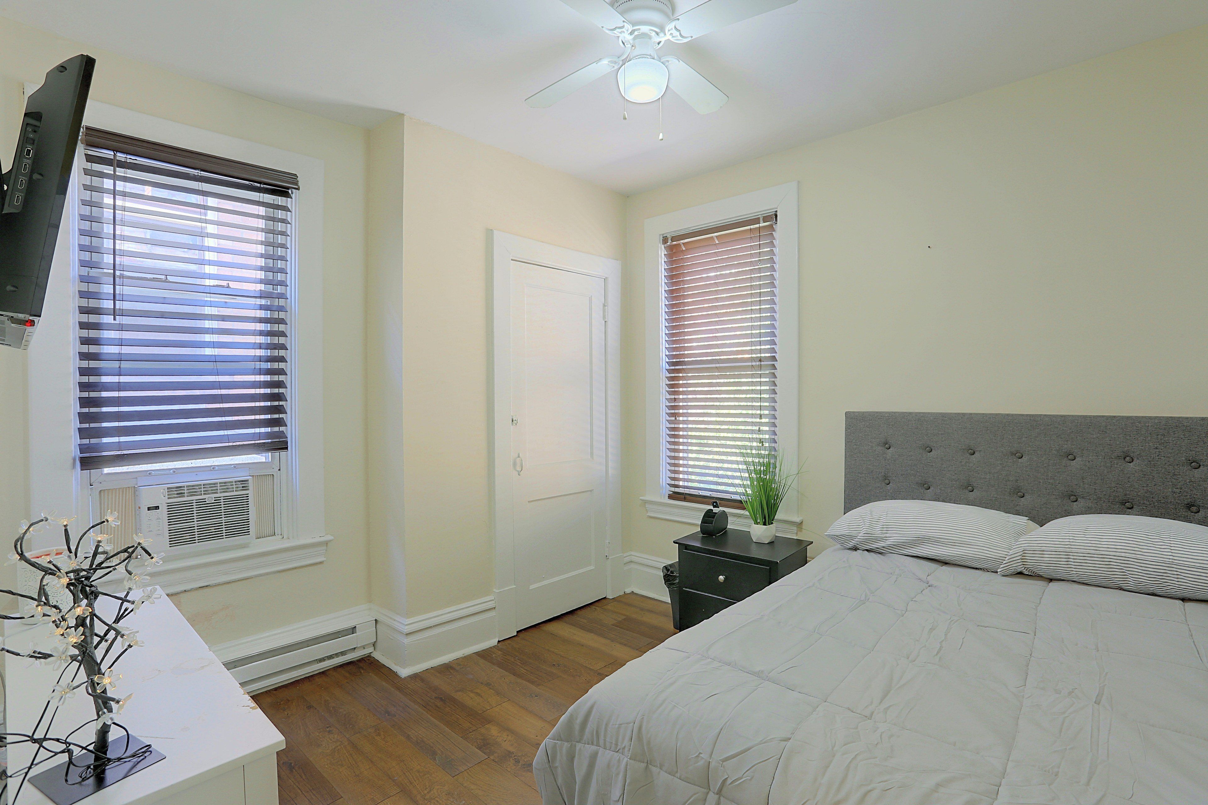 A bedroom with a bed, bedside table, nightstand, and a ceiling fan.