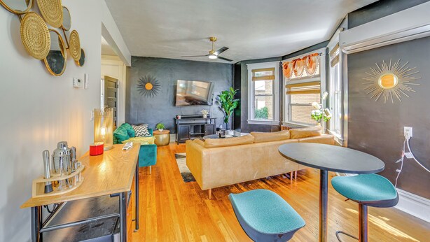 A modern living room with a sofa, a coffee table, and a TV. There is a ceiling fan, a fireplace, and a window with curtains. - Dog-friendly Pittsburgh Home, 3 Mi to Downtown! (Pittsburgh)