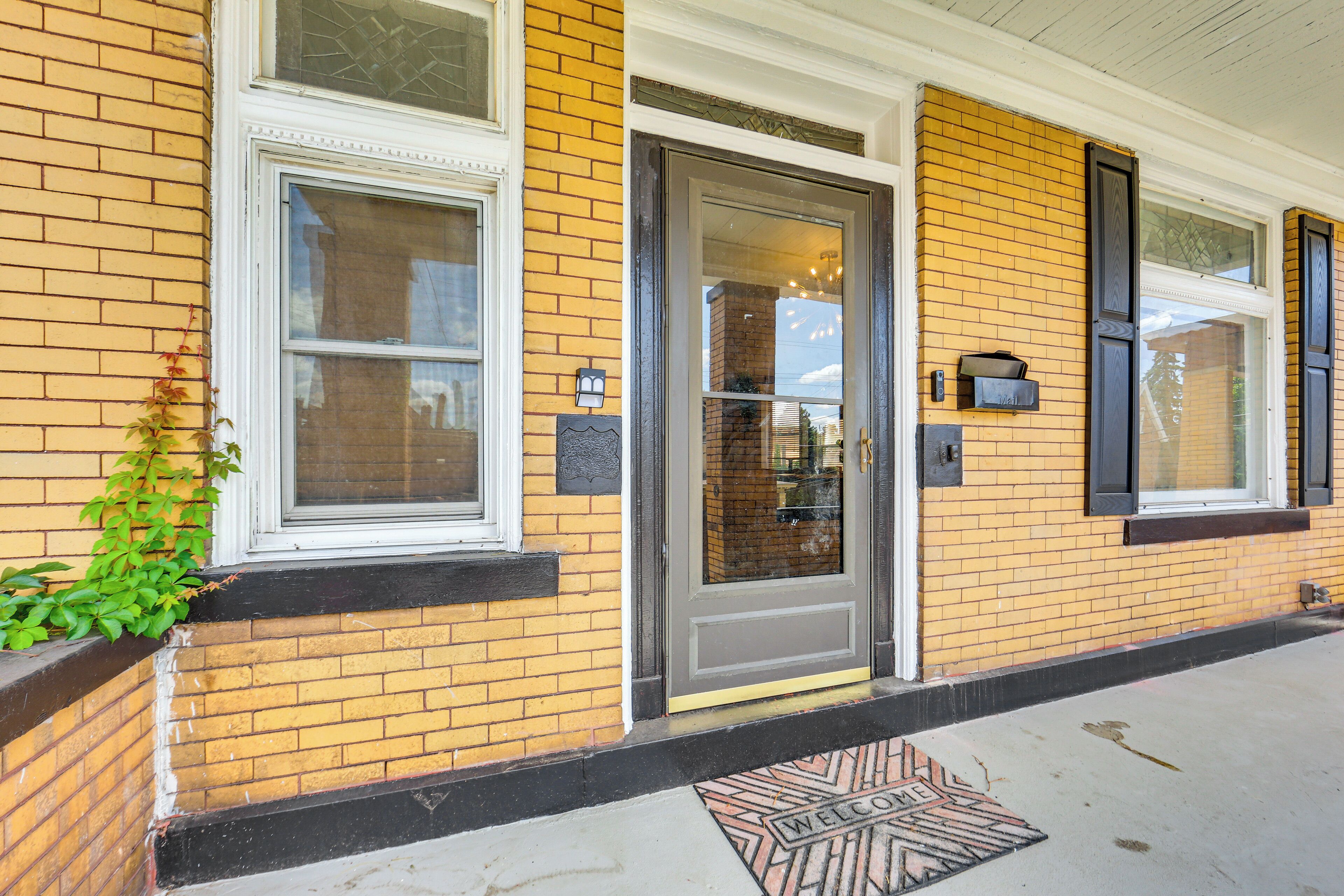 A yellow brick building with a gray door, white window frames, and a welcome mat at the entrance.