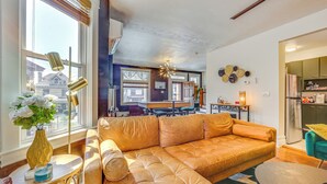 A living room with a large leather sofa, a small side table with a vase, and a view of the kitchen and dining area through the window. - Dog-friendly Pittsburgh Home, 3 Mi to Downtown! (Pittsburgh)