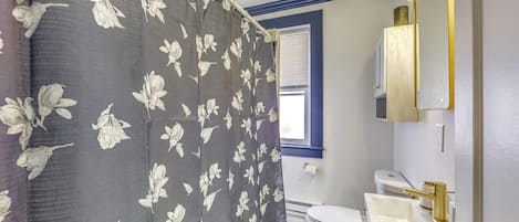 A bathroom with a shower curtain, toilet, sink, and mirror.