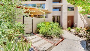 Un immeuble moderne à plusieurs étages, doté d’une cour dallée, d’un espace extérieur aménagé pour s’asseoir et de diverses plantes.