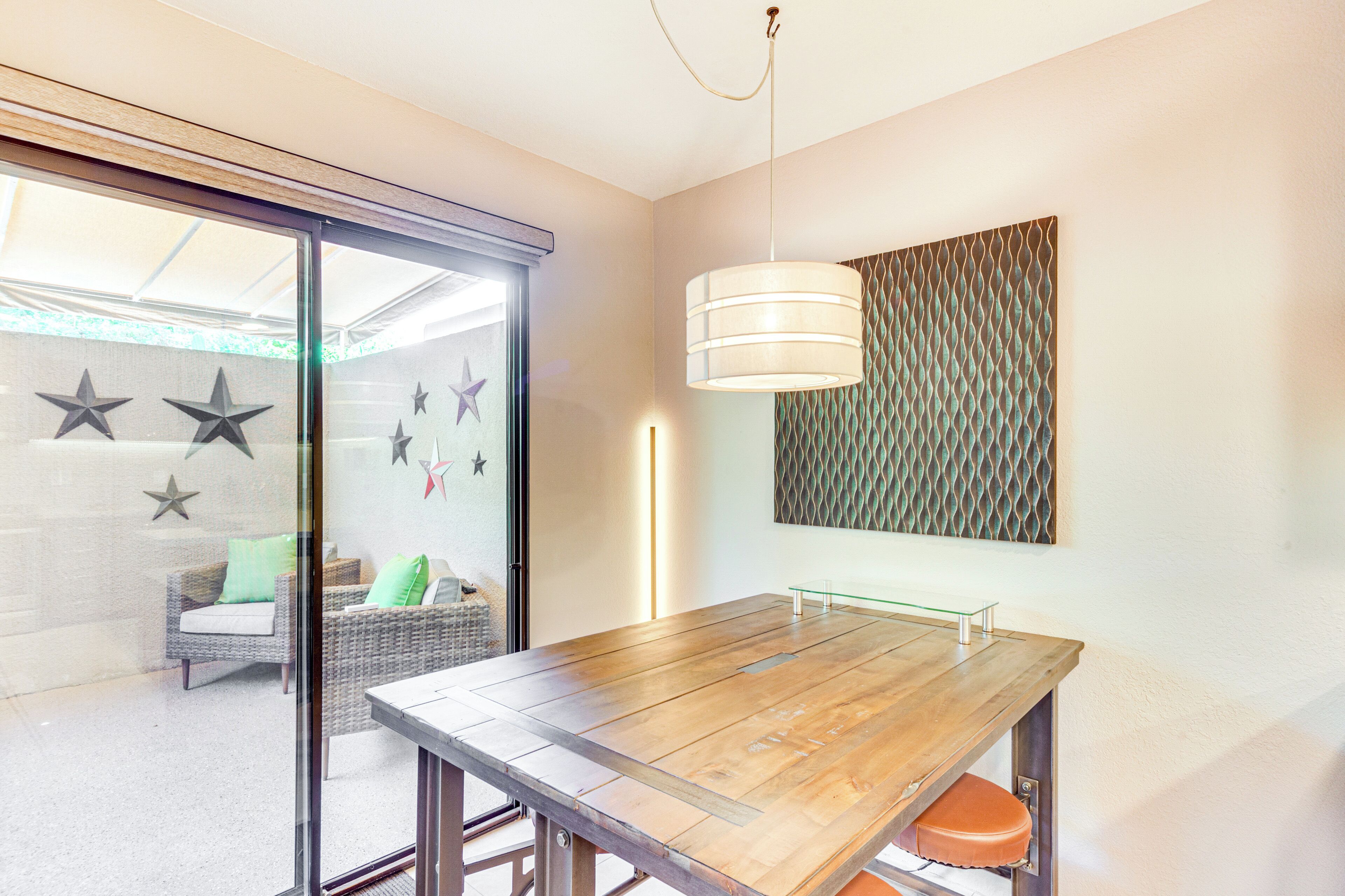 Un comedor con mesa de madera, separador de vidrio, sillas de mimbre y lámpara fijada a la pared.