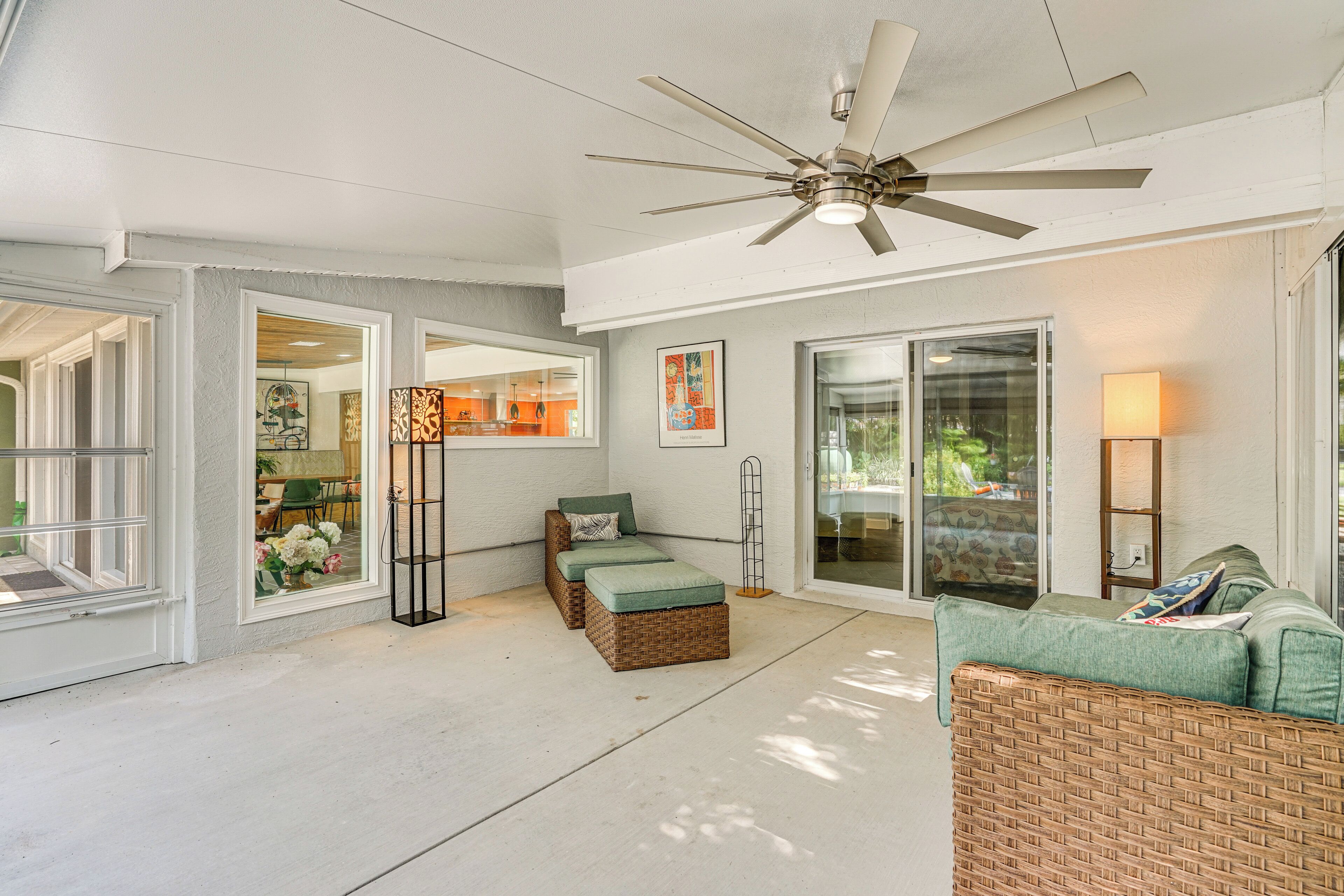 Un patio coperto con ventilatore a soffitto, mobili in vimini e vista attraverso le porte in vetro.