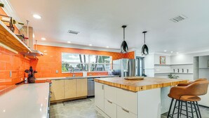 Une cuisine moderne dotée d’un îlot central, d’un pare-feu orange et offrant une vue sur l’extérieur.