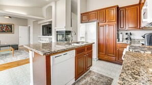 Uma cozinha moderna com bancadas de granito, armários de madeira e eletrodomésticos de aço inoxidável.
