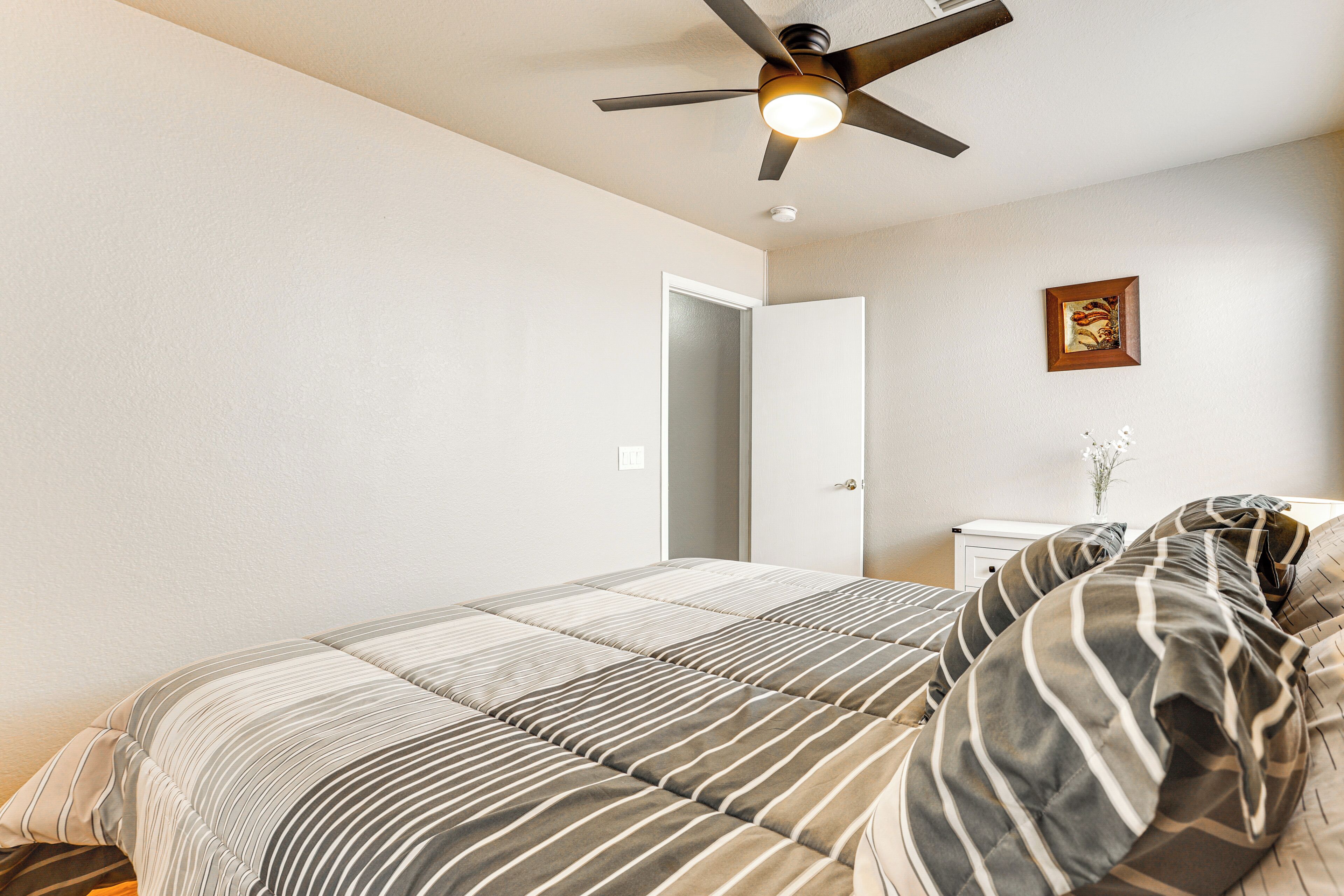 Ein Schlafzimmer mit einem Bett, einem Deckenventilator, einem Nachttisch und einer Tür.
