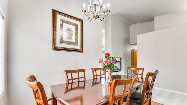 Comedor con mesa y sillas de madera, una araña y un cuadro en la pared.