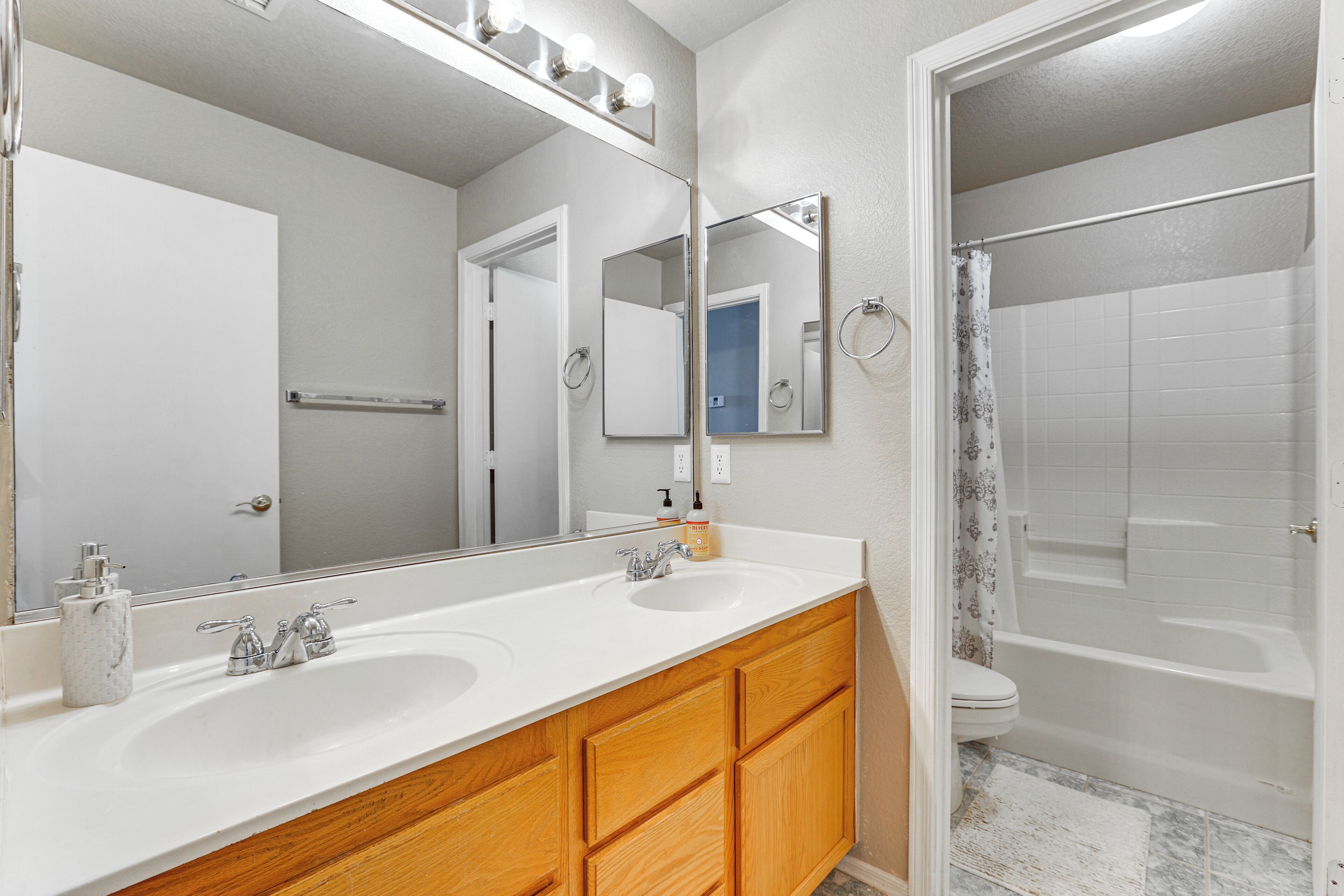 A bathroom with a double sink vanity, a large mirror, and a shower area.