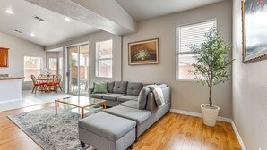 Uma sala de estar ampla com sofá modular, uma mesa de centro e um espaço de jantar com cadeiras.