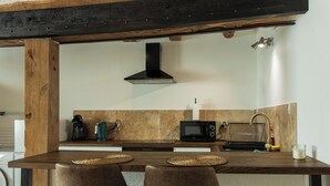 Une cuisine avec un îlot central en bois, une hotte aspirante noire, un four à micro-ondes et une bouilloire.