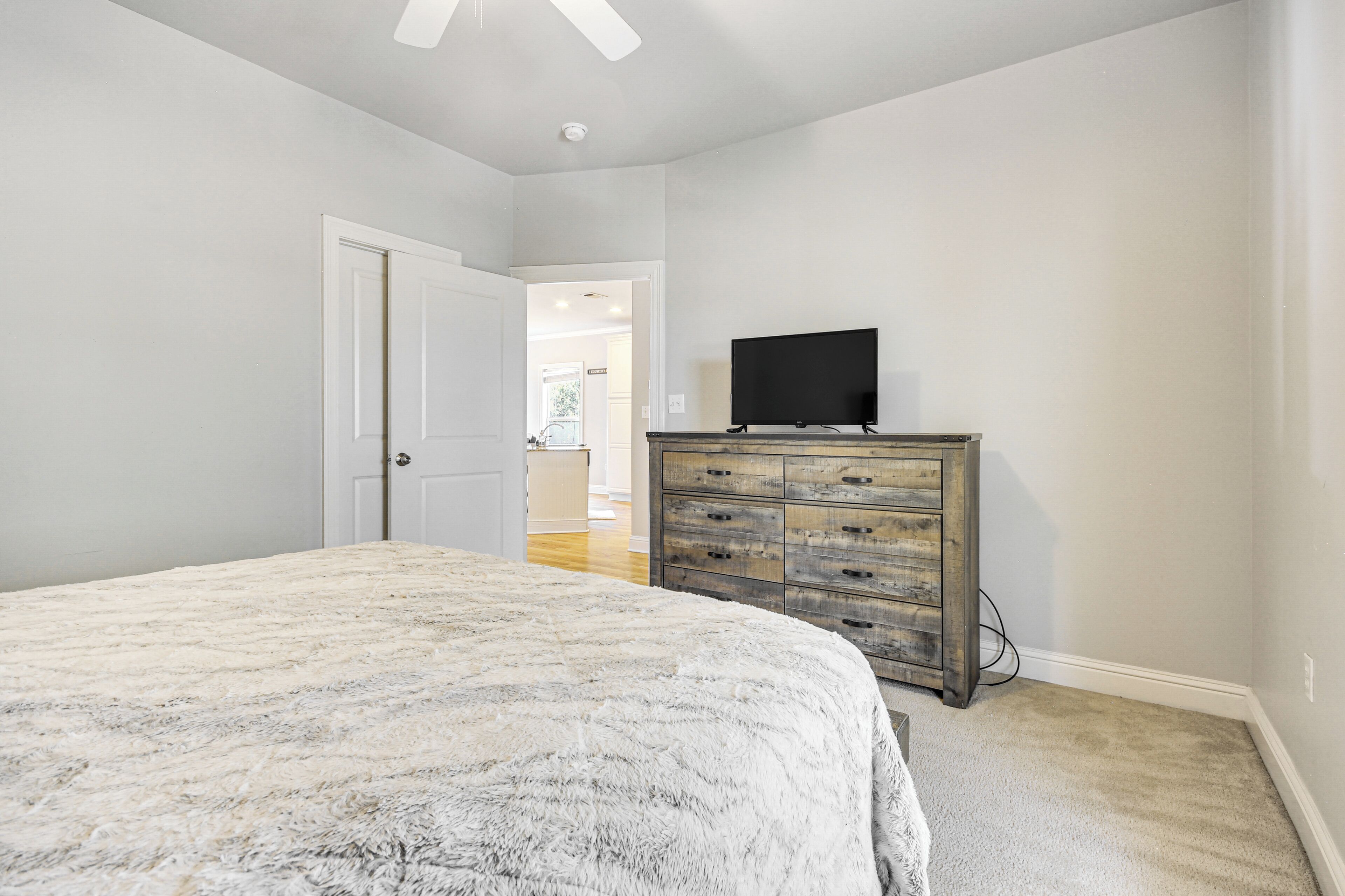Une chambre avec un grand lit, une commode en bois et un téléviseur posé sur le dessus.