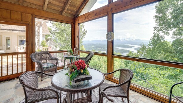 Habitación con piso de madera, mobiliario de mimbre y una mesa de vidrio, con vistas a un paisaje pintoresco.