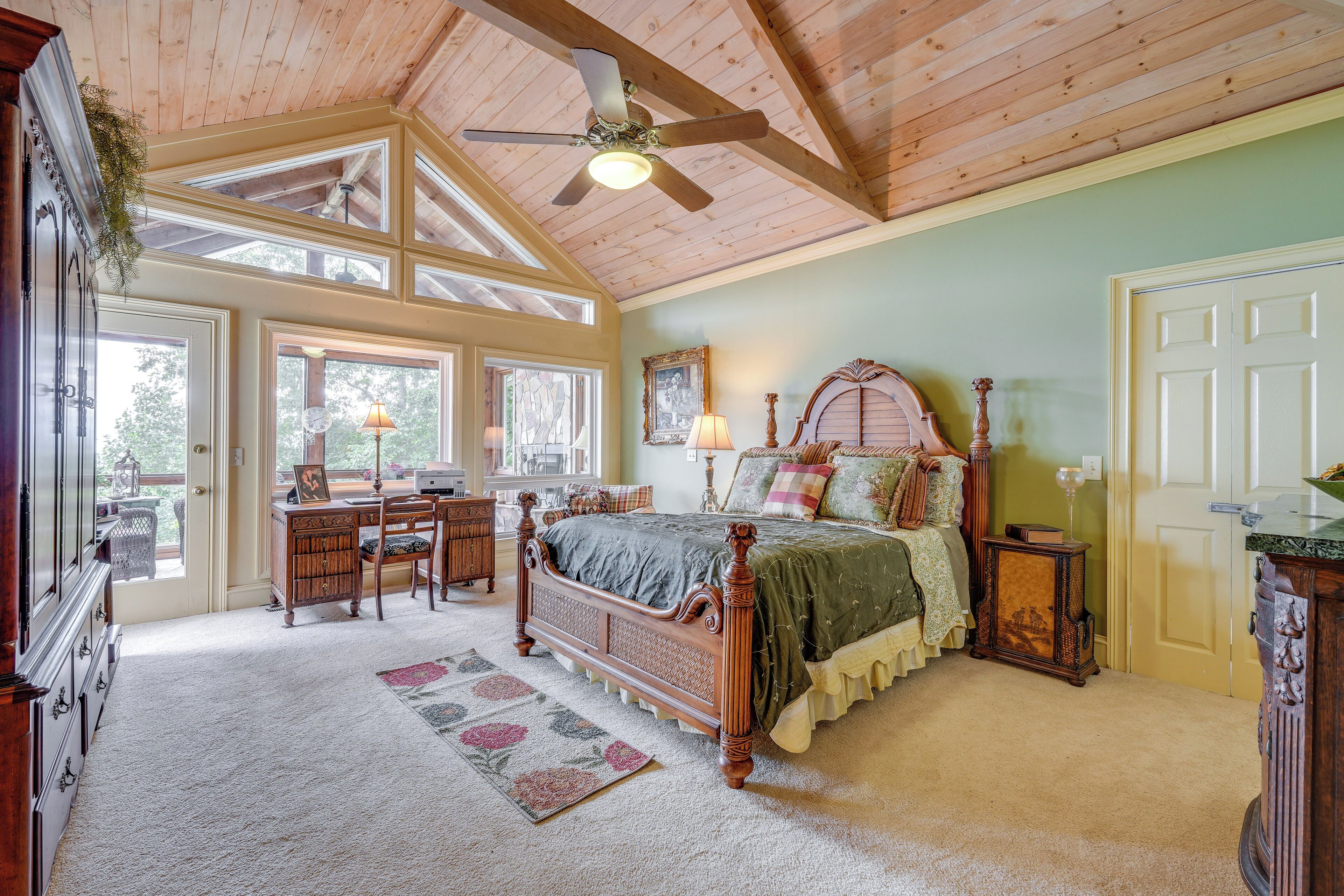 A bedroom with a wooden ceiling, a large bed, a desk, and a chair.