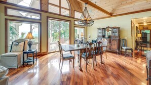 Una habitación amplia con techo de madera, ventanas grandes, una mesa de comedor con sillas y un candelabro.