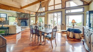 Un comedor amplio con mesa y sillas de madera, chimenea de piedra y ventanas grandes que ofrecen vistas al exterior.