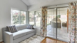 A modern living room with a grey sofa, patterned curtains, and large windows offering a view of the outdoors. - Huntington Beach Home: Fire Pit, Grill + More! (Huntington Beach)