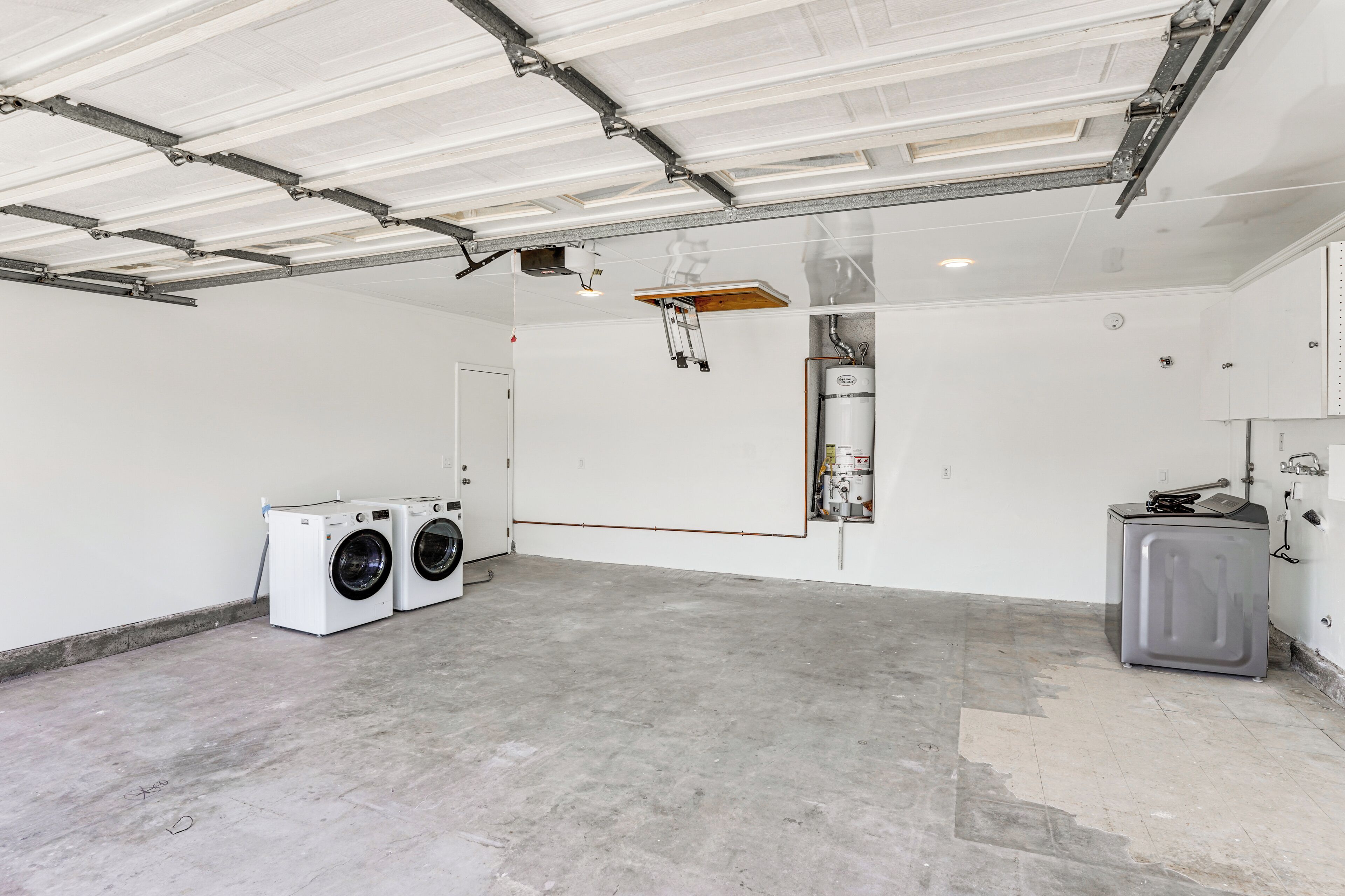Eine geräumige Garage mit Betonboden, einer Waschmaschine, einem Trockner und einem Hauswirtschaftsraum mit Warmwasserbereiter.