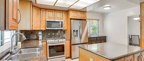 A modern kitchen with wooden cabinets, stainless steel appliances, a granite countertop, and a large island.