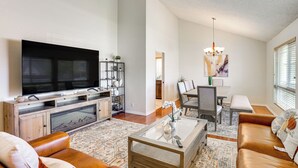 A modern living room with a flat-screen TV, leather sofa, coffee table, and a dining area with a chandelier. - Huntington Beach Home: Fire Pit, Grill + More! (Huntington Beach)