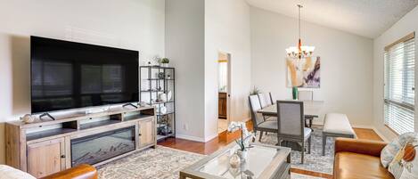 A modern living room with a flat-screen TV, leather sofa, coffee table, and a dining area with a chandelier.