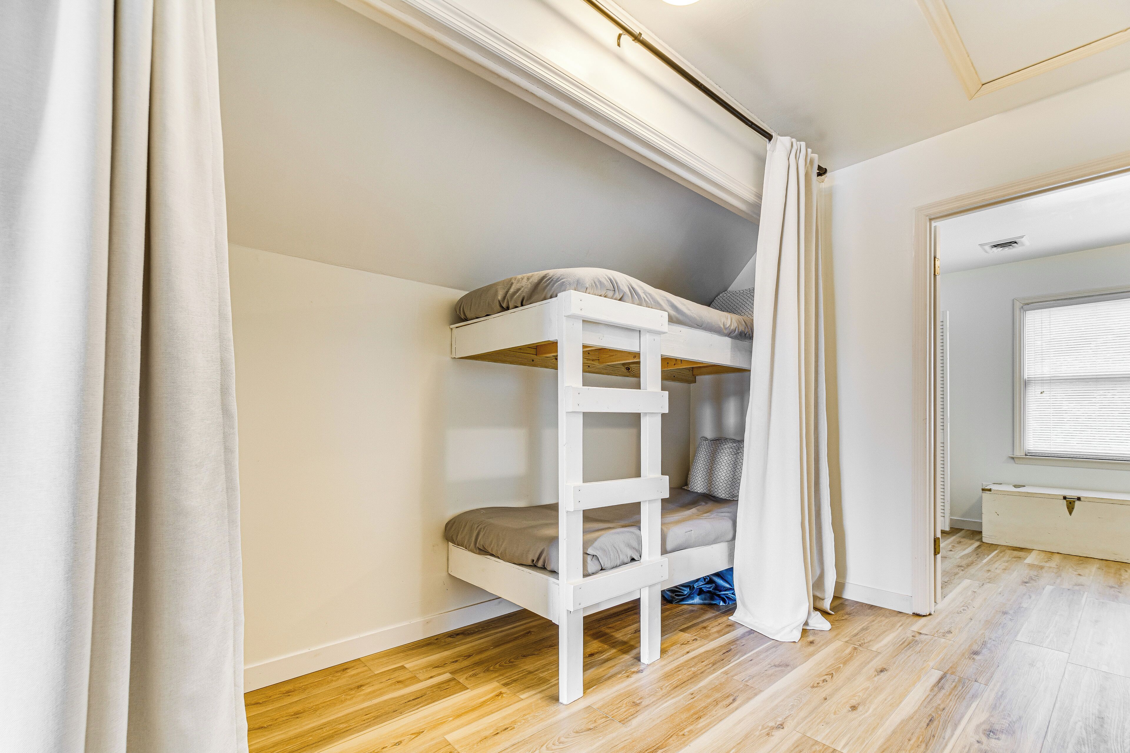 Una cama litera en una habitación con suelo de madera, una ventana con persianas y una puerta que da a otra habitación.