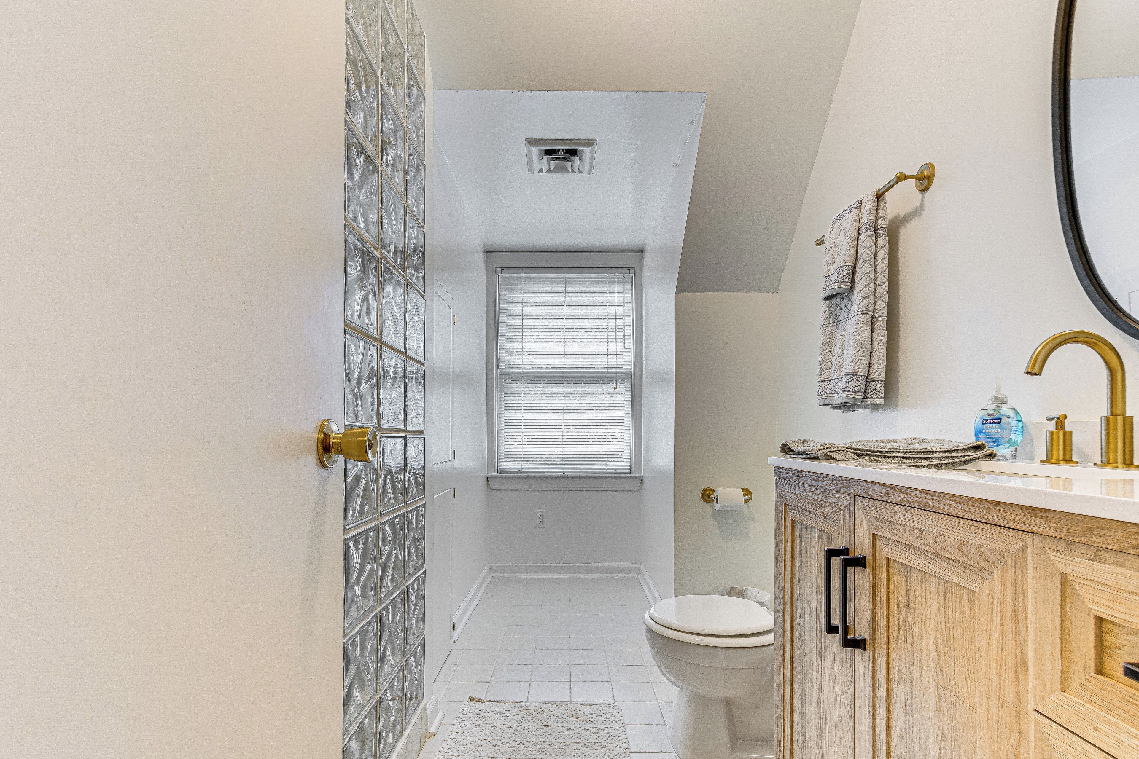 A bathroom with a toilet, a sink with gold fixtures, and a window with blinds.