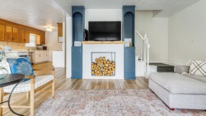 A living room with a fireplace, a sofa, a dining table, and a kitchen in the background. - Private Island Getaway in Roanoke Rapids w/ Grill! (Roanoke Rapids)
