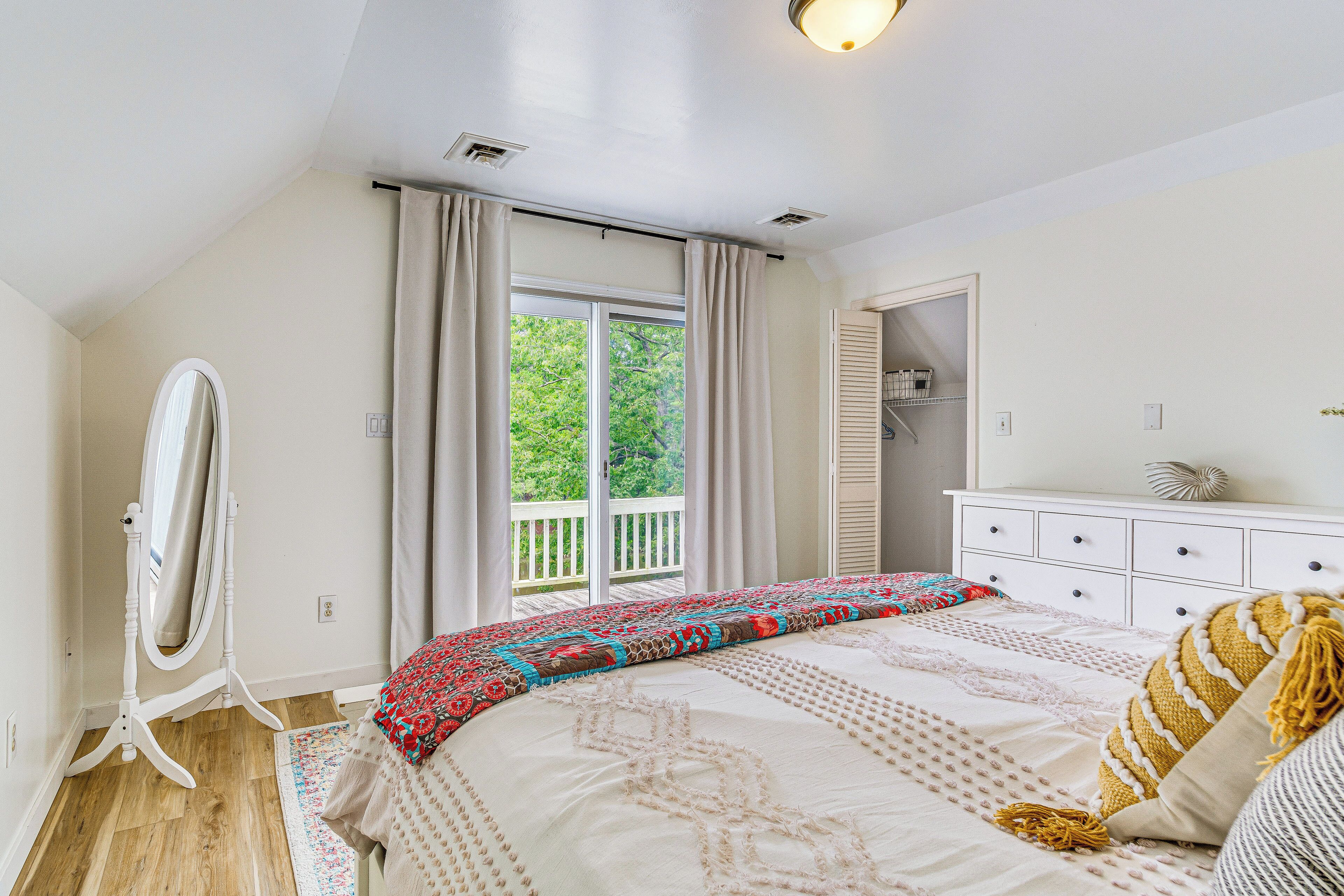 A bedroom with a large bed, a dresser, a mirror, and a window with curtains.
