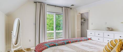A bedroom with a large bed, a dresser, a mirror, and a window with curtains.