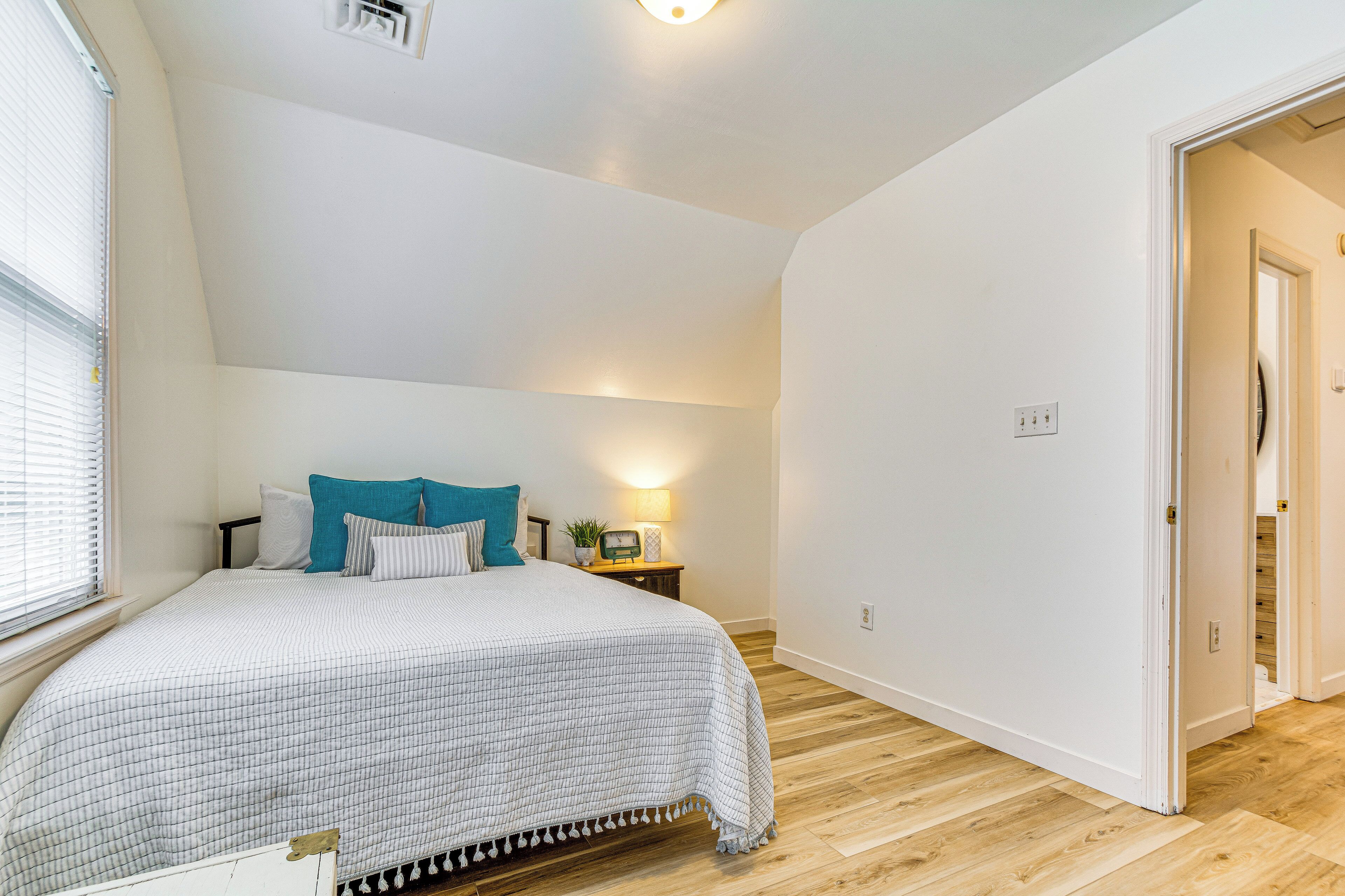 A bedroom with a bed, bedside table, lamp, and a door leading to another room.