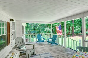 Une véranda couverte avec des balustrades en bois, deux fauteuils Adirondack, une table et un drapeau américain.