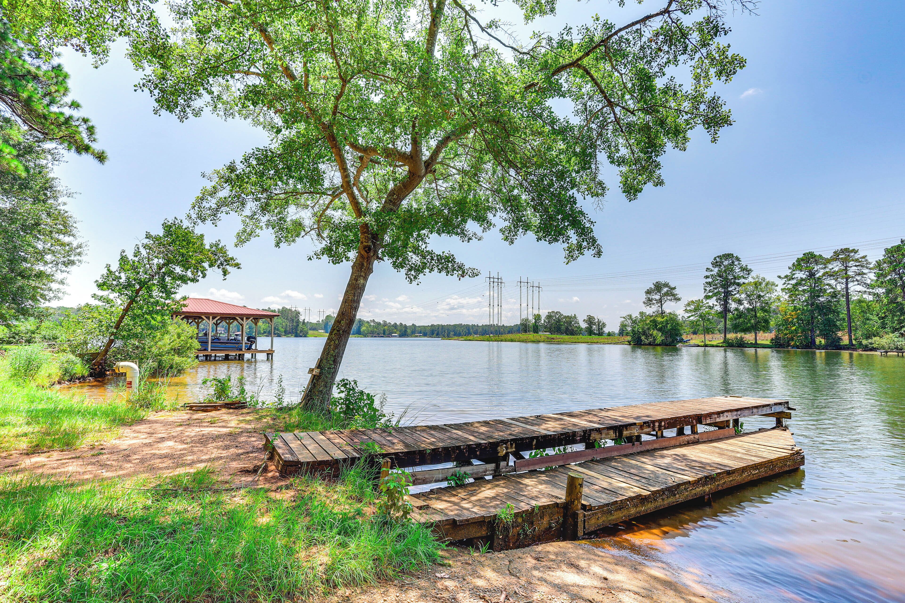 A wooden dock extending into a calm lake, surrounded by lush greenery and a small pavilion.