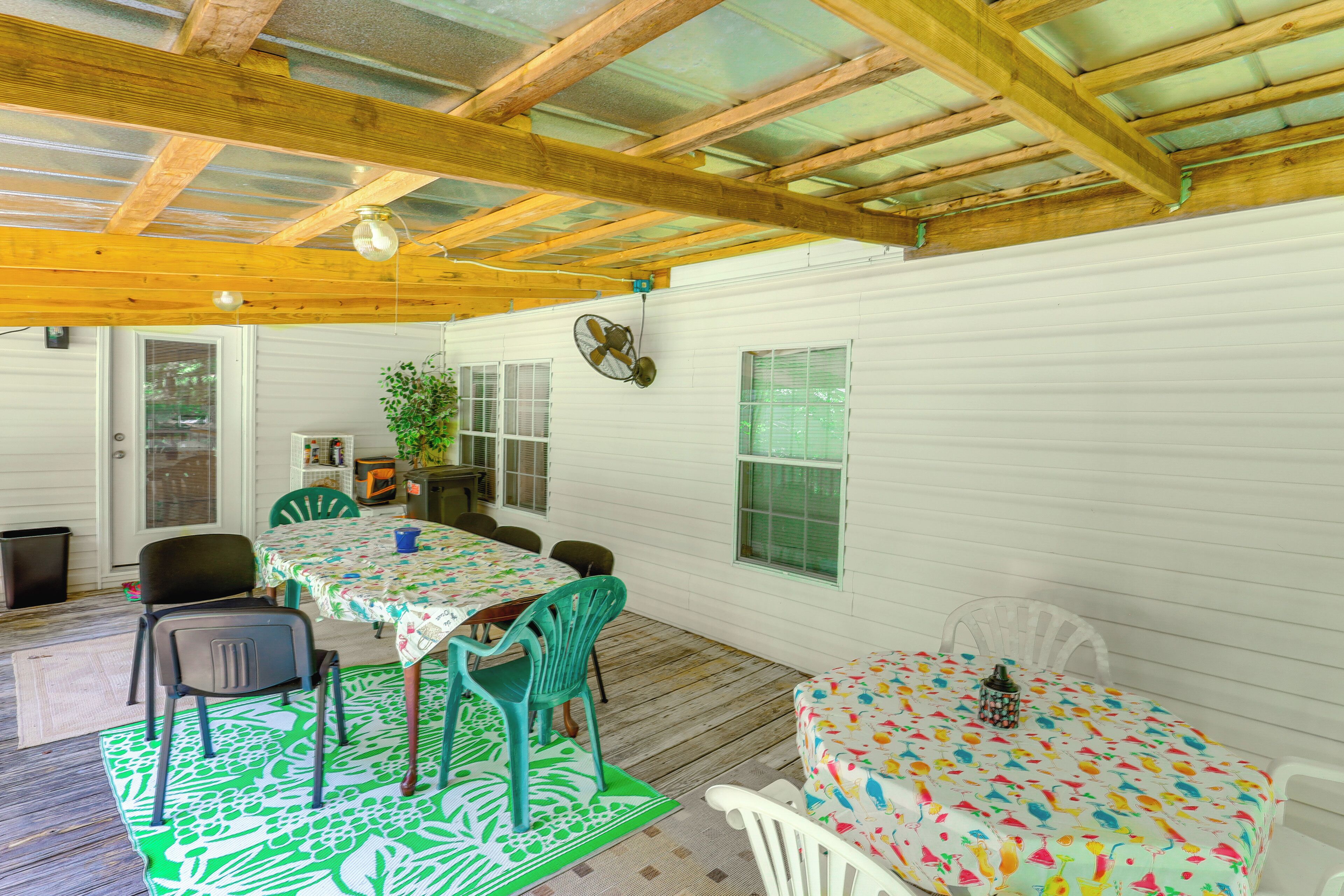 A covered patio with wooden beams, a table with a colorful tablecloth, and green chairs.
