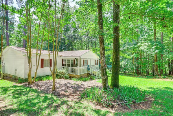 A small, single-story cabin with a porch, surrounded by a forested area. - Pet-friendly Sparta Retreat: Porches & Fire Pit! (Milledgeville)