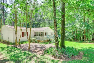 A small, single-story cabin with a porch, surrounded by a forested area.