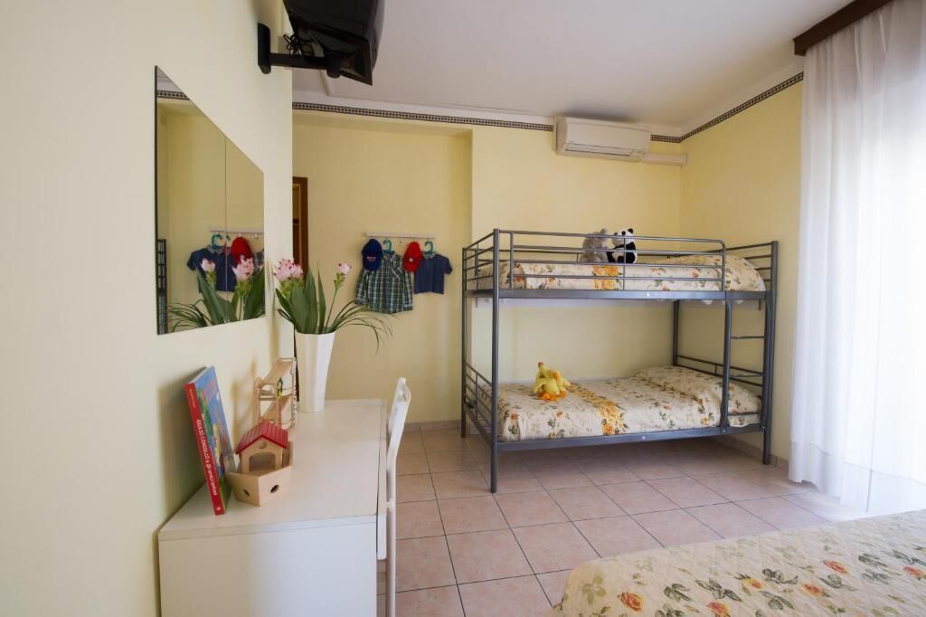 Una habitació amb un llit superposat, un escriptori amb una cadira, un mirall i una planta en test.