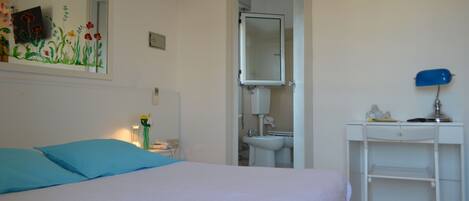 A bedroom with a bed, a bedside table, a mirror, a sink, and a desk.