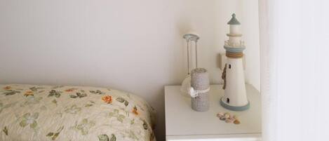 A bed with floral bedding, a nightstand with a lamp and a decorative lighthouse, and a small pile of seashells.