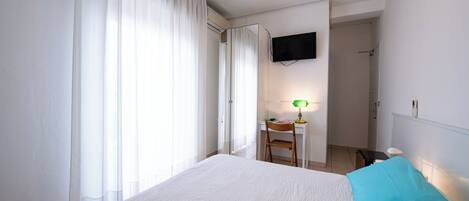 A hotel room with a large bed, a desk with a chair, a television mounted on the wall, and a window with curtains.
