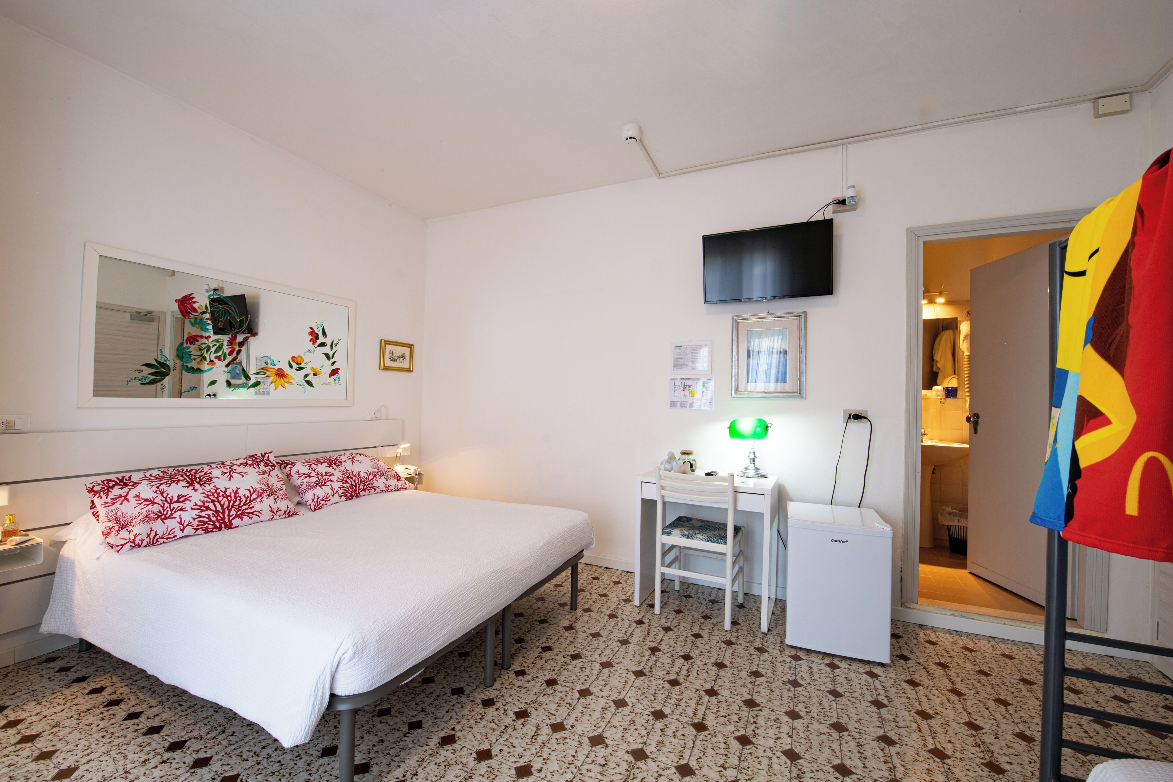 A hotel room with a bed, a desk, a small refrigerator, a television, and a door leading to a bathroom.