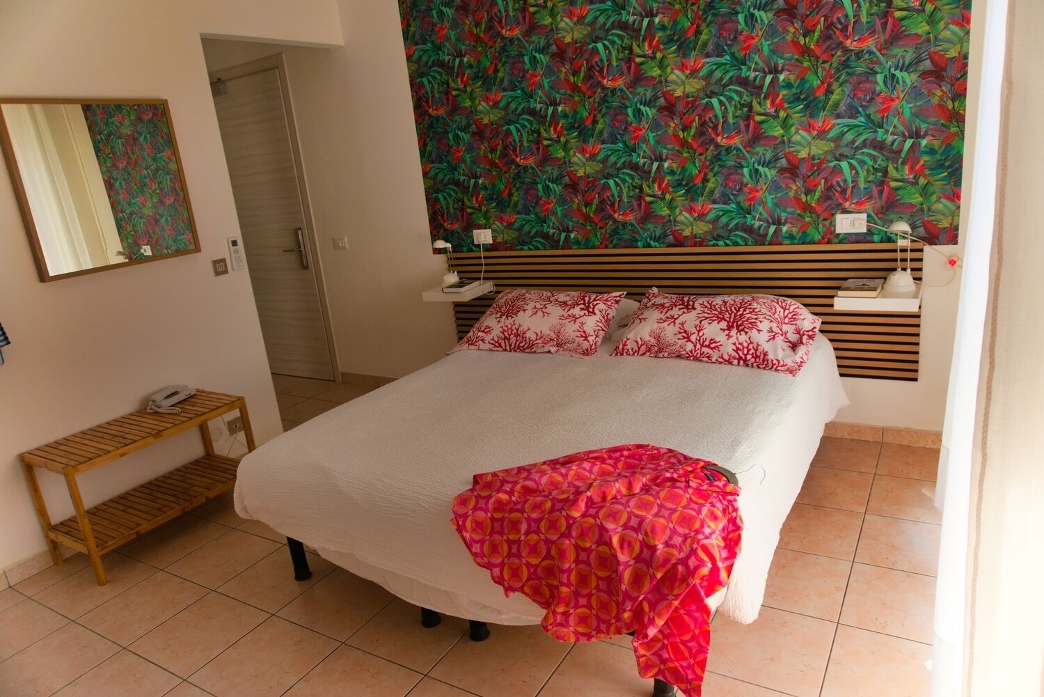 Une chambre à coucher avec un lit, un banc en bois, un mur orné d’une fresque florale et une porte.
