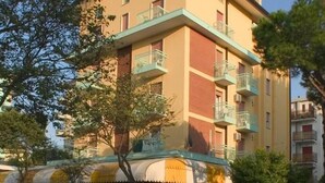 A multi-story building with balconies, a covered outdoor seating area, and a street in front. - Le Petit Hotel (Lido di Jesolo)